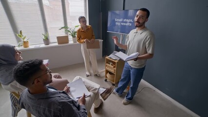 Biracial male student speaking confidently in front of classmates as standing by screen displaying motivational quote and teacher guiding him, practicing public speaking during English lesson