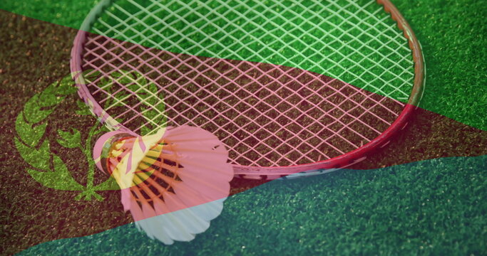Displaying badminton racket with shuttlecock resting on turf court, showing flag stripe overlays