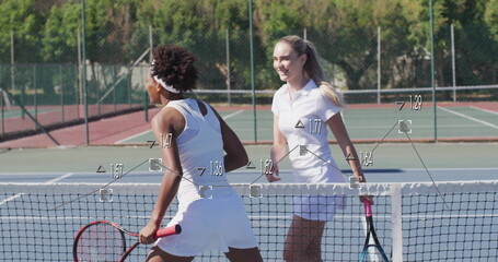Meeting two women wearing white tennis gear, headband leaning over net at sunny court, with rackets