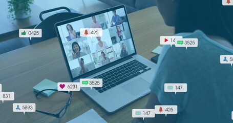 Viewing laptop showing nine remote team members at home desk with eyeglasses, floating social icons