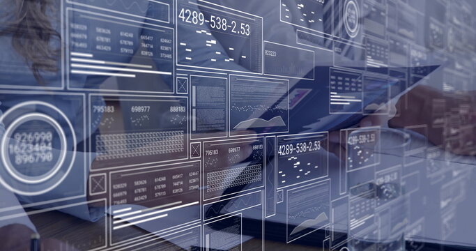 Typing analyst wearing white shirt on laptop beside colleague using tablet at desk with data panels