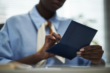 Black woman holding customers passport while sitting at desk in bank office, focusing on document and preparing paperwork, hands and partial face visible, business environment implied