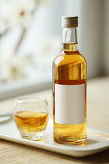 bottle of japanese plum wine with elegant minimal label, placed on a clean white ceramic tray, next to a small glass filled with golden liquid