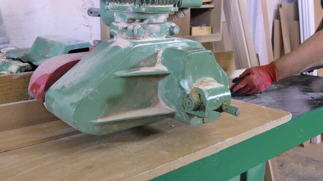 A worker shapes a plank on a band saw, hands close up.