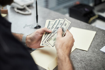 Hands of unrecognizable man counting US dollar bills at bank office desk, holding cash in hands...