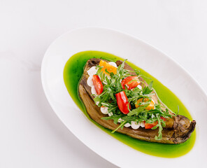 Grilled eggplant with salad topped by herbs and dressing on a plate