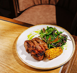 Grilled steak served with salad and corn on a wooden table