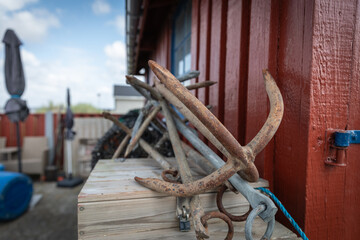 Close up of rusty old boat anchors leaning against a red wooden fishing hut

