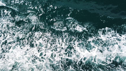 Ocean's Rhythmic Symphony: High-angle perspective captures the intricate texture and movement of the ocean. The water, a dynamic canvas of blues and whites.