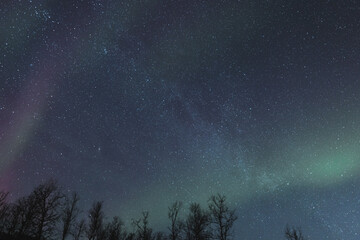 Colourful sky full of green and purple aurora borealis with Milky way over frozen lake. Norwegian sky show