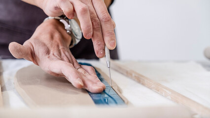 A close-up shot of a middle-aged woman artist shaping clay with sculpting tools at a table in an...