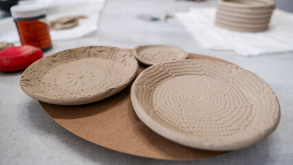 In an art studio with an environment adorned with artistic paintings in the background, handmade clay plates with lace patterns are displayed on a table