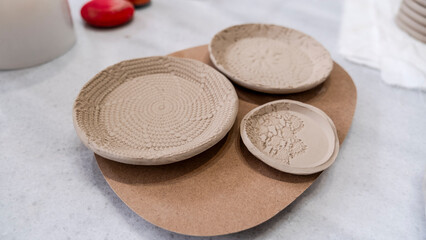 In an art studio with an environment adorned with artistic paintings in the background, handmade clay plates with lace patterns are displayed on a table