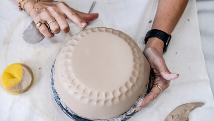 A close-up shot of a middle-aged woman artist shaping clay with sculpting tools at a table in an...