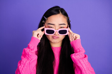 Naklejka premium Fashionable young woman in stylish pink sweater with sunglasses posing against a violet background, trendy candid aesthetic