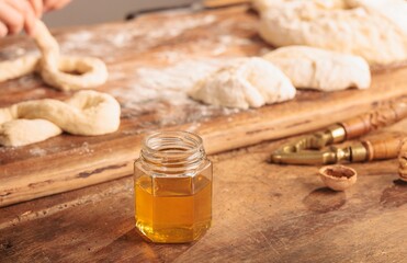A baker gently shapes dough into the figure-eight forms of Mucenici on a floured board, while a jar of golden honey and walnuts suggest a sweet finish to this Romanian Spring treat