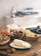 On a weathered counter, eggs, flour, walnuts, vanilla, lemon zest, and butter are arranged. Ingredients readied for the comforting bake of traditional Mucenici