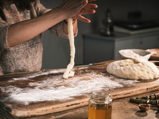 A baker gently stretches and shapes dough on a floured wooden board. Preparing Mucenici, a traditional Romanian pastry, brings warmth and heritage to the kitchen