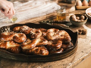 A hand delicately sprinkles chopped nuts onto freshly baked Mucenici, arranged on a rustic wooden tray, alongside honey, eggs, and walnuts, inviting a taste of Romanian heritage