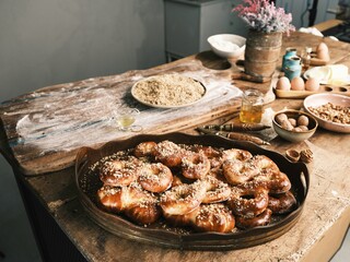 Golden-brown Mucenici are presented on a rustic wooden surface, surrounded by ingredients like flour, walnuts, and honey, evoking a sense of home baking and tradition