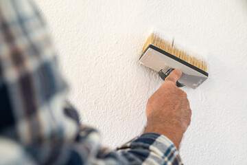 Close-up of a hand. A painter paints a masonry wall with white paint using using the paintbrush. Construction industry. 