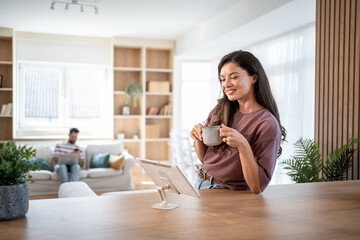 Woman drinking coffee and using tablet at home