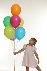 Cute little girl in dress with bunch of colorful balloons on white background