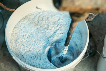 Production of decorative plaster at the factory. Materials for repair and decoration. Closeup of blue decorative plaster mixture in a bowl showcasing texture and contrast.