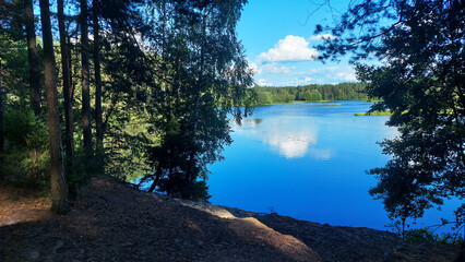 Obraz premium Serene lakeside view with lush trees reflecting in the calm water under a blue sky