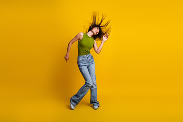 Young stylish woman dancing enthusiastically in a casual outfit against a yellow background, displaying vibrant energy