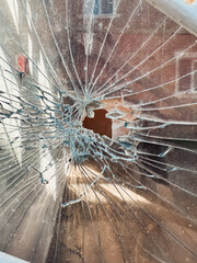 Obraz premium Shattered glass with intricate cracks and a central hole, capturing the impact and texture of broken material in a well-lit indoor environment