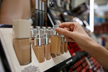 A woman is reaching for a bottle of foundation on a store shelf