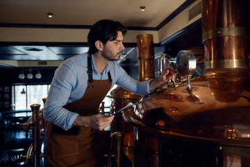 Confident brewer man wearing an apron is diligently working in a brewery setting