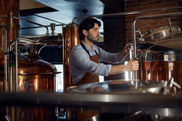 A brewer man worker wearing an apron is diligently working in a local brewery