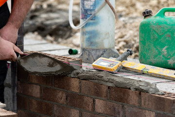 Bricklayer constructing stone wall using bricks, cement mortar mix and trowel