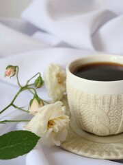 Fresh white roses placed beside a cup of hot black coffee, creating a romantic and serene composition.