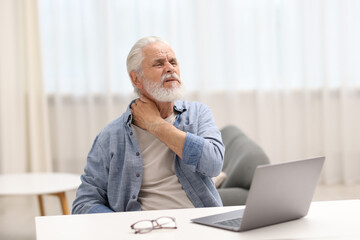 Fototapeta premium Senior man suffering from neck pain at table indoors