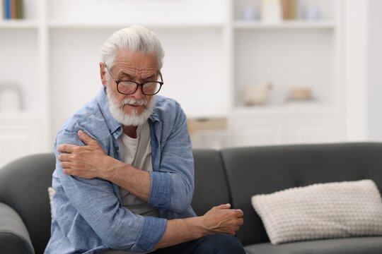 Senior man suffering from shoulder pain at home, space for text