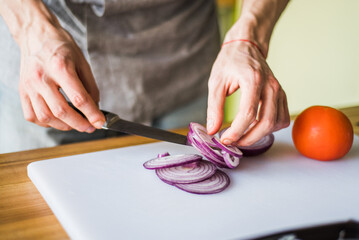 Hands cutting onion and radish for fresh vegetable salad.