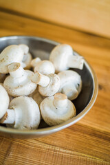 Fresh white mushrooms in a metal bowl on wooden background.