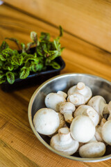 Fresh white mushrooms in a metal bowl on wooden background.