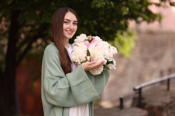 Fototapeta premium Charming woman with bouquet of beautiful peonies on city street