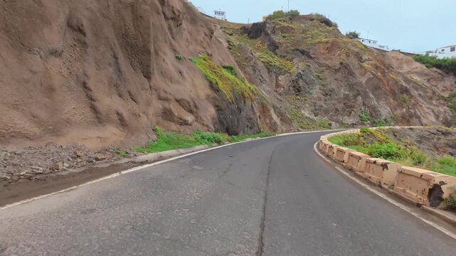 A winding coastal road meanders through steep cliffs, flanked by vibrant greenery and stunning ocean views