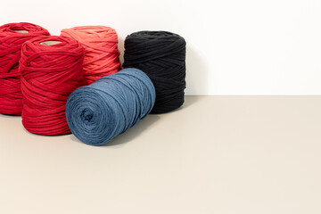 Background of a group of Spools of recycled t-shirt yarn arranged on a beige table against a white wall. Copy space