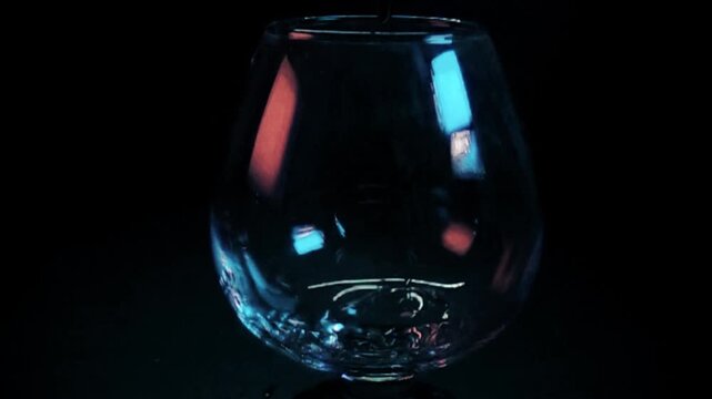 Clear liquid pouring into a snifter glass on black background