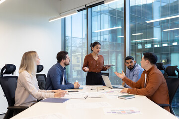 Professionals engaged in a discussion during a team meeting in a well-lit office with large windows, demonstrating collaboration, teamwork, and effective communication.