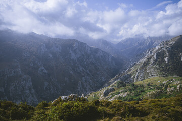 Dramatic view of Picos de Europa mountain range with rugged limestone peaks, deep valleys, and scattered green meadows under a partly cloudy sky in northern Spain