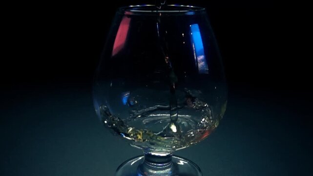 Pouring golden liquid into a snifter glass on dark background