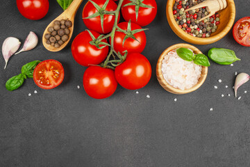 Fresh ripe tomatoes on the vine with garlic cloves, basil leaves, pink Himalayan salt, whole allspice, and a bowl of colorful peppercorns on a dark stone background, top view. copy space