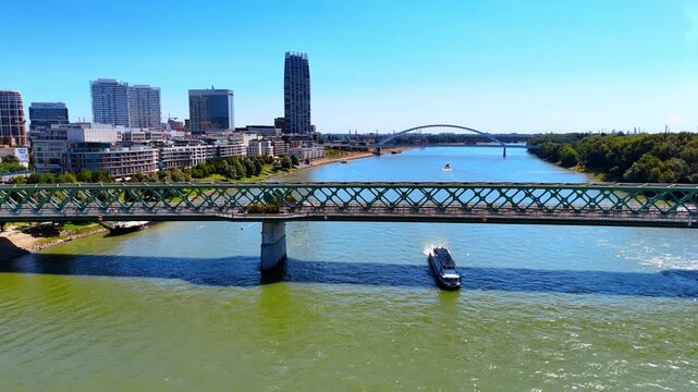 The Old Bridge connecting the banks of the Danube. A riverboat passes under the bridge. Skyline of Bratislava and the Appolo Bridge at backdrop.